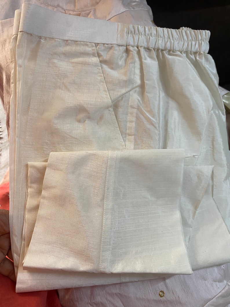 May include: White cotton pants with a drawstring waistband and a folded cuff. The pants are made of a lightweight fabric and have a subtle sheen.