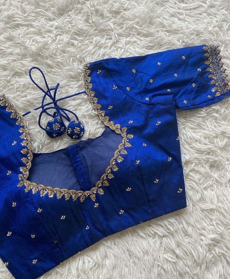 May include: A royal blue embroidered blouse with gold trim and sequins. The blouse has a scoop neckline and short sleeves.