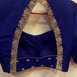 Op de afbeelding: Een koninklijk blauwe blouse met een sleutelgatrug en gouden borduurwerk. Het borduurwerk is een delicaat bloemenpatroon dat langs de halslijn loopt en naar beneden langs de rug.