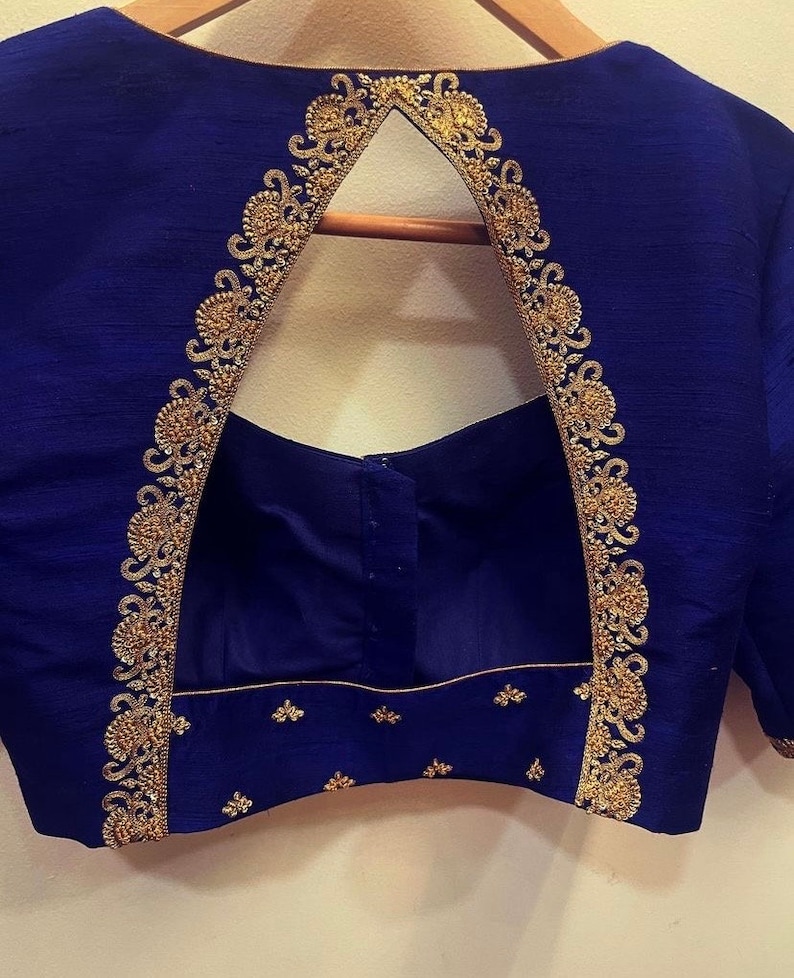 Op de afbeelding: Een koninklijk blauwe blouse met een sleutelgatrug en gouden borduurwerk. Het borduurwerk is een delicaat bloemenpatroon dat langs de halslijn loopt en naar beneden langs de rug.