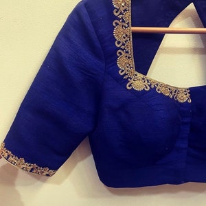 Op de afbeelding: Een koninklijk blauwe zijden blouse met gouden borduurwerk rond de halslijn en mouwen. De blouse heeft een ronde halslijn en een keyhole rug.