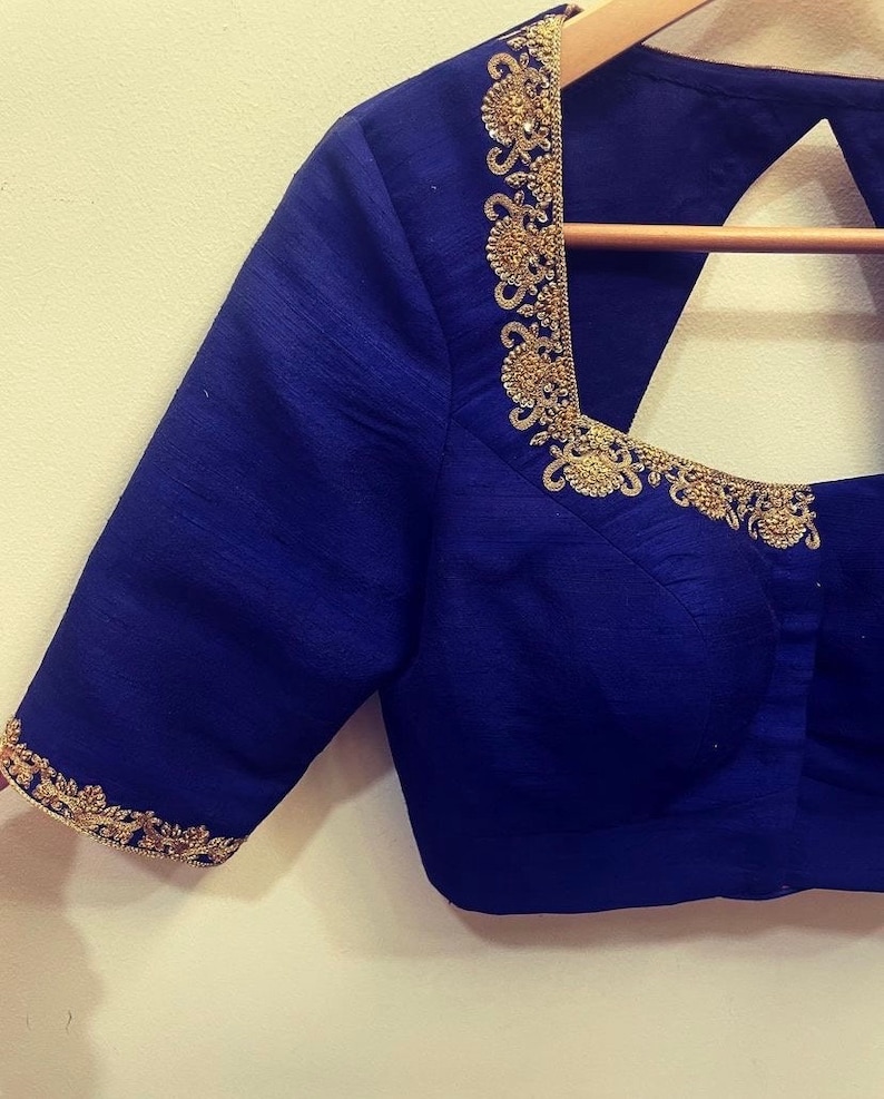 Op de afbeelding: Een koninklijk blauwe zijden blouse met gouden borduurwerk rond de halslijn en mouwen. De blouse heeft een ronde halslijn en een keyhole rug.