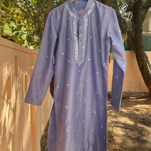 K&ouml;nnte beinhalten: Eine hellblaue Kurta mit einem silbernen Spiegelarbeitsdesign. Die Kurta hat einen Knopfverschluss am Hals und lange &Auml;rmel.