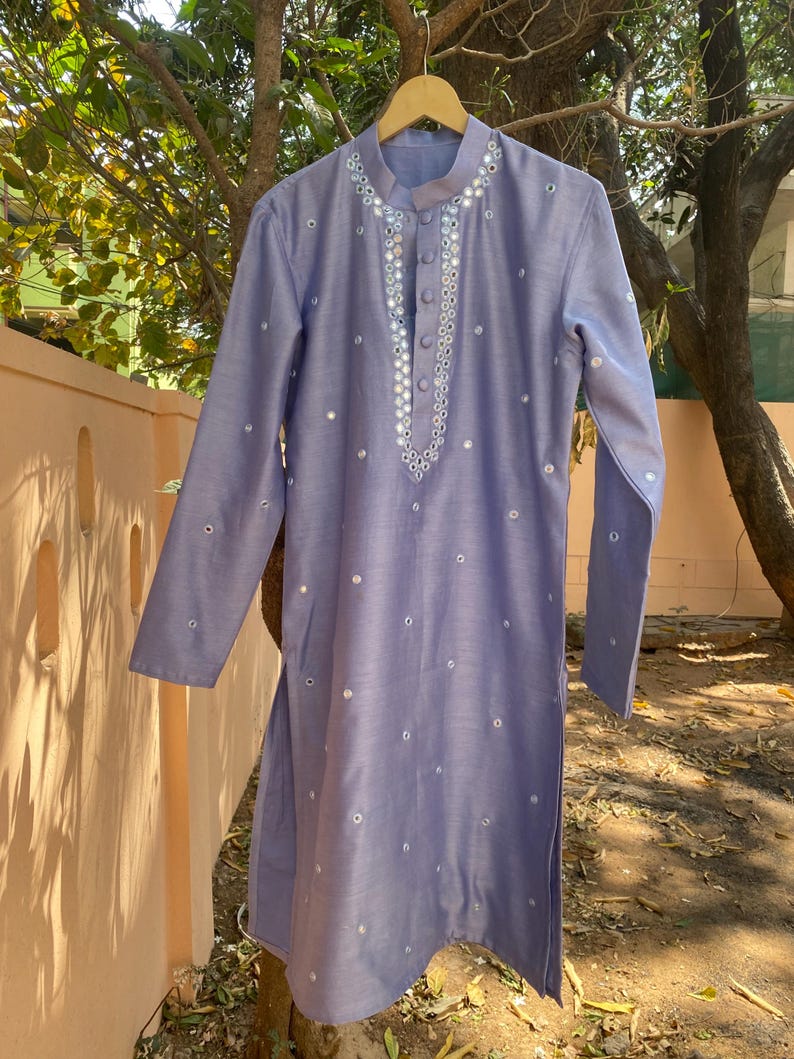 K&ouml;nnte beinhalten: Eine hellblaue Kurta mit einem silbernen Spiegelarbeitsdesign. Die Kurta hat einen Knopfverschluss am Hals und lange &Auml;rmel.