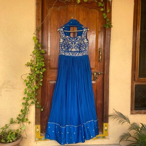 May include: A royal blue maxi dress with gold embroidery and a sleeveless design. The dress has a pleated skirt and a fitted bodice.