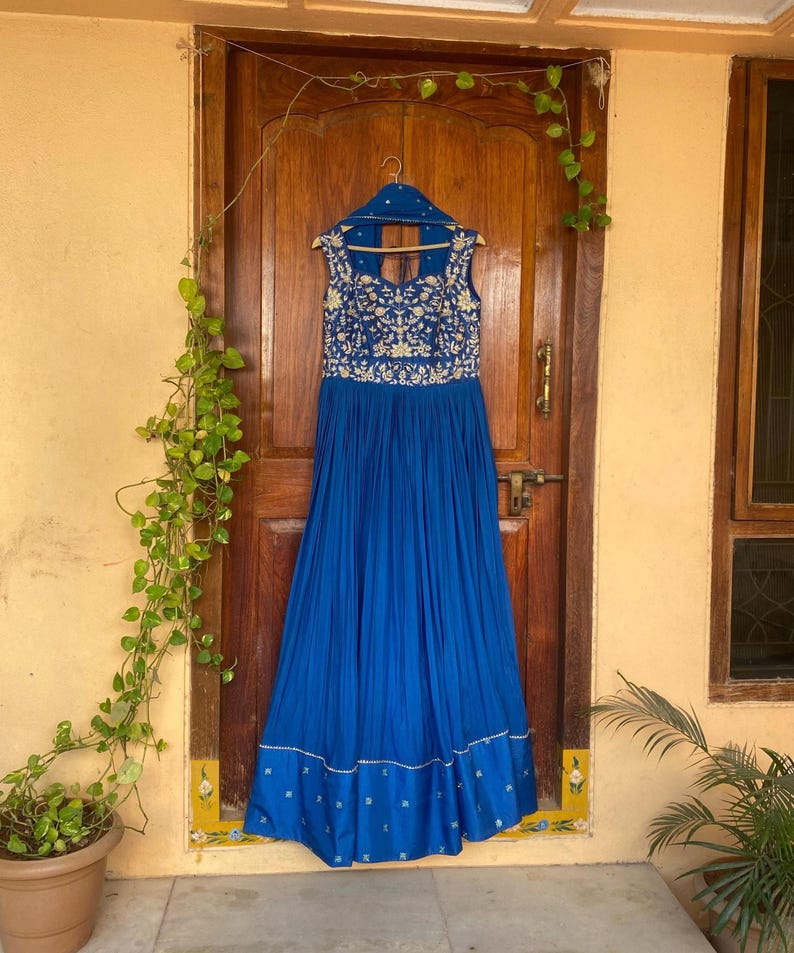 May include: A royal blue maxi dress with gold embroidery and a sleeveless design. The dress has a pleated skirt and a fitted bodice.