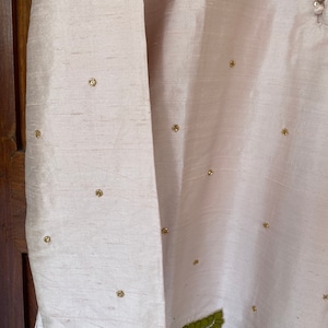 May include: A pale pink garment with gold embellishments. The garment has long sleeves and a decorative design on the bottom.