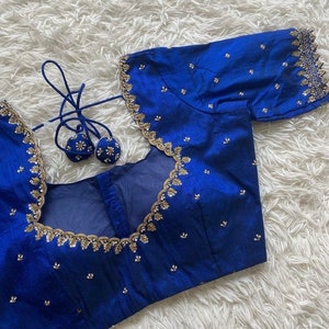 May include: A royal blue embroidered blouse with gold trim and sequins. The blouse has a scoop neck and short sleeves.
