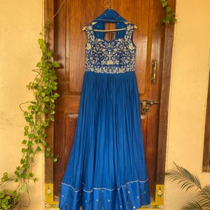 May include: A long, royal blue dress with a sleeveless bodice and a gathered skirt. The dress is embroidered with gold floral patterns and has a small, open back.