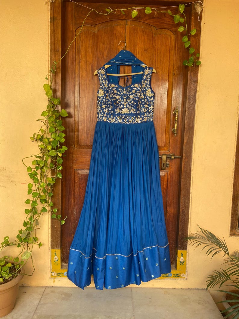 May include: A long, royal blue dress with a sleeveless bodice and a gathered skirt. The dress is embroidered with gold floral patterns and has a small, open back.