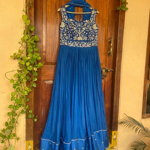 May include: A long, royal blue dress with gold embroidery and a matching dupatta. The dress has a sleeveless bodice and a flowing skirt.