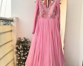 Puede incluir: Un vestido rosa de manga larga con escote en V y falda de capas. El corpiño está adornado con bordados florales y lentejuelas.