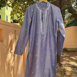 K&ouml;nnte beinhalten: Eine hellblaue Kurta mit Knopfverschluss und aufwendiger Spiegel-Stickerei. Die Kurta hat lange &Auml;rmel und ist mit kleinen runden Spiegeln verziert.