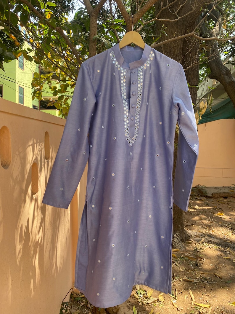 K&ouml;nnte beinhalten: Eine hellblaue Kurta mit Knopfverschluss und aufwendiger Spiegel-Stickerei. Die Kurta hat lange &Auml;rmel und ist mit kleinen runden Spiegeln verziert.