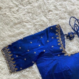 May include: A royal blue silk blouse with gold and silver embroidery. The blouse has a scalloped neckline and short sleeves.