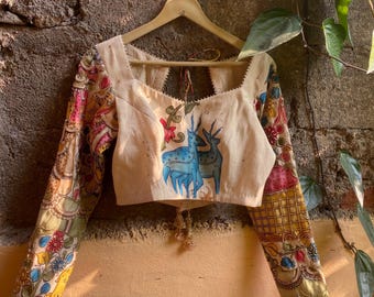 May include: A white cotton blouse with long sleeves and a square neckline. The sleeves and neckline are trimmed with a decorative stitch. The blouse features a hand-painted design of two blue deer on the front. The sleeves are decorated with a colorful floral pattern.