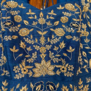 May include: A blue fabric with gold embroidery of floral designs. The fabric has a slight sheen and is likely silk or satin.