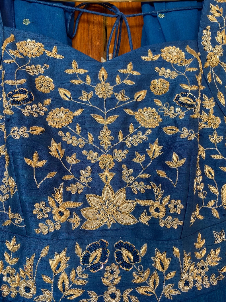 May include: A blue fabric with gold embroidery of floral designs. The fabric has a slight sheen and is likely silk or satin.