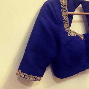 Op de afbeelding: Een koninklijk blauwe blouse met gouden borduurwerk rond de halslijn en mouwen.