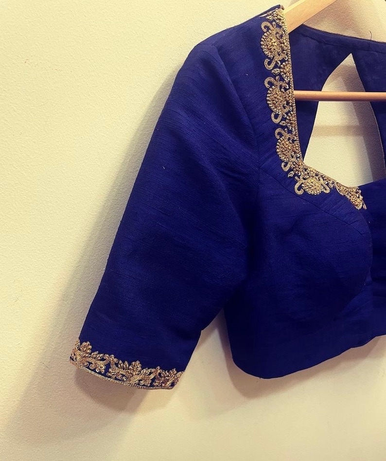 Op de afbeelding: Een koninklijk blauwe blouse met gouden borduurwerk rond de halslijn en mouwen.