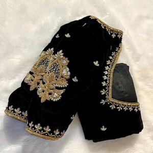 May include: A black velvet blouse with gold and silver embroidery. The blouse has a high neckline and long sleeves.
