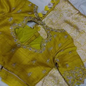 May include: A yellow embroidered blouse with a keyhole neckline and silver embellishments. The blouse is paired with a silver and white patterned fabric.