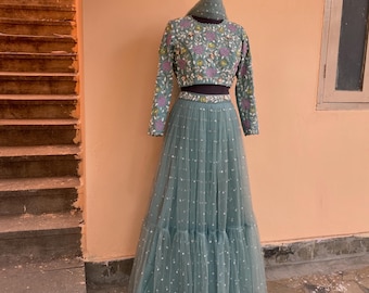 May include: A teal blue embroidered crop top with long sleeves and a matching tulle skirt with a dotted pattern and ruffled layers.