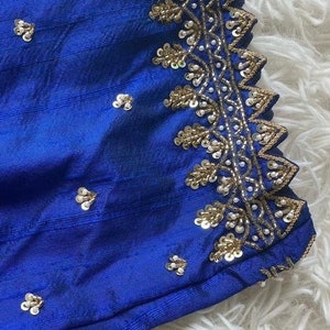 May include: Close-up of a royal blue fabric with gold and white embellishments. The fabric has a textured surface and is decorated with a border of sequins and beads.