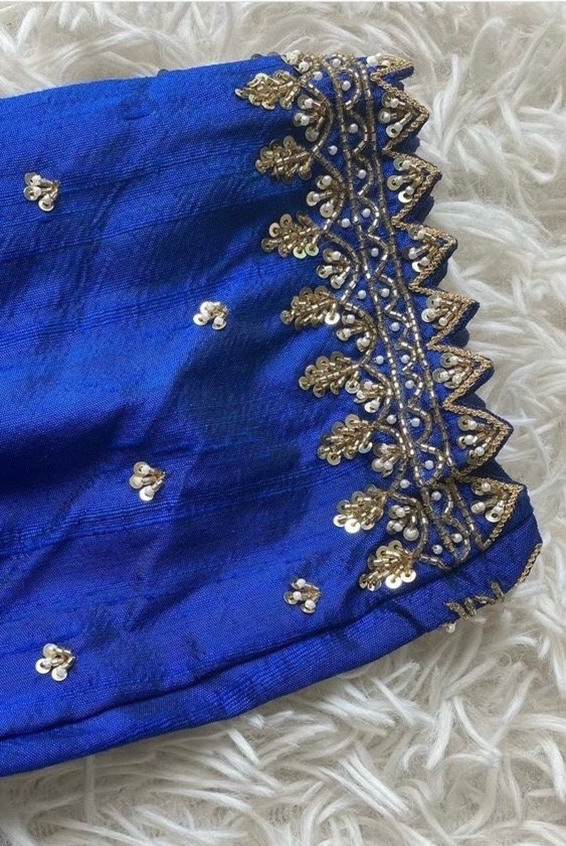May include: Close-up of a royal blue fabric with gold and white embellishments. The fabric has a textured surface and is decorated with a border of sequins and beads.