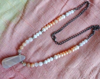 May include: A necklace featuring a gradient of white, peach, and orange beads. The necklace has a silver chain and a large, teardrop-shaped pendant.