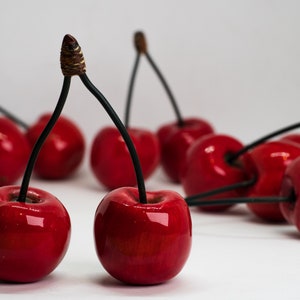 Puede incluir: Un grupo de cerezas rojas con tallos negros. Las cerezas están dispuestas en una fila, con los tallos apuntando en diferentes direcciones.