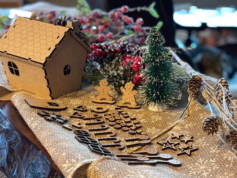 Pu&ograve; includere: Un kit di casetta di pan di zenzero in legno marrone con un pino innevato, due omini di pan di zenzero e vari ritagli di legno per decorare. Il kit include stelle, fiocchi di neve, foglie e altre forme festive.