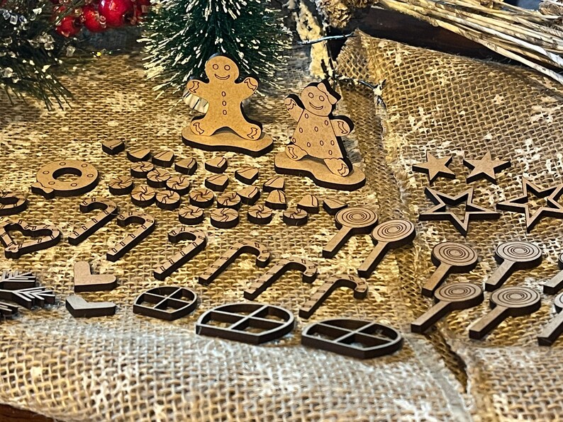 Pu&ograve; includere: Una collezione di addobbi natalizi in legno, tra cui omini di pan di zenzero, bastoncini di zucchero, stelle e una ciambella. Gli addobbi sono dipinti di marrone e hanno un aspetto rustico.