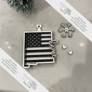 Puede incluir: Un adorno de bandera estadounidense en blanco y negro con la palabra "home" recortada en el centro. El adorno está diseñado para ser cortado en una Glowforge. El adorno está acompañado por un copo de nieve y dos corazones.