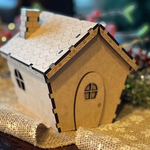 Pu&ograve; includere: Una piccola casa di legno con un tetto marrone e un camino. La casa ha una porta e una finestra. La casa &egrave; decorata con un motivo floreale.