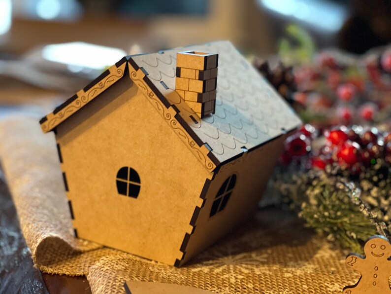 Pu&ograve; includere: Una piccola casa di legno marrone con un camino e un tetto nero. La casa ha due finestre ed &egrave; decorata con dettagli intricati.