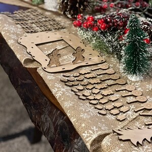 Pu&ograve; includere: Un calendario dell'avvento natalizio in legno con una casetta di pan di zenzero, omini di pan di zenzero e un albero di Natale. Il calendario ha 24 porte numerate, ciascuna con un piccolo ornamento in legno dietro. Gli ornamenti includono bastoncini di zucchero, campane, stelle e altre forme festive.