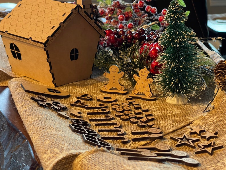 May include: A wooden gingerbread house kit with a small Christmas tree, two gingerbread people, and a variety of wooden cutouts, including stars, snowflakes, and swirls.