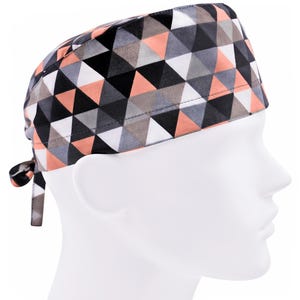 May include: A surgical scrub hat with a geometric pattern in shades of pink, gray, black, and white. The hat has a tie at the back.