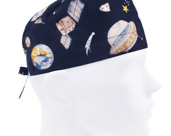 Könnte beinhalten: Eine marineblaue OP-Mütze mit einem Weltraum-Motiv, das Planeten, Sterne und ein Raumschiff zeigt. Die Mütze hat einen Bindegurt auf der Rückseite.