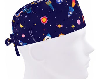 Könnte beinhalten: Eine blaue OP-Mütze mit einem Weltraum-Motiv mit Raketen, Planeten, Sternen und einer Sonne.