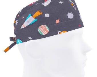 Könnte beinhalten: Eine graue OP-Mütze mit einem Weltraum-Motiv mit Planeten, Sternen und einer Rakete. Die Mütze hat einen seitlichen Knoten.