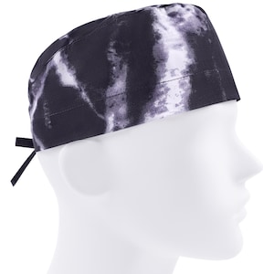 May include: A scrub cap featuring a black and white tie-dye pattern with a marbled effect. The cap has a rounded crown, a wide band around the base, and two fabric ties extending from the back to allow for an adjustable fit around the head.