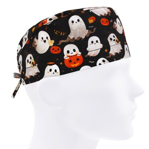 May include: Black Halloween-themed scrub cap featuring a pattern of white ghosts, orange jack-o'-lanterns, and small orange stars. The cap has a tie closure and is designed to fit comfortably. The fabric is dark with a repeating pattern.