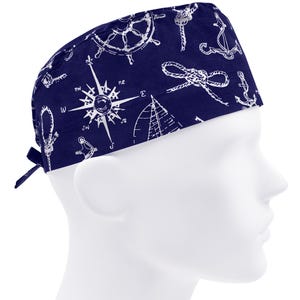 May include: A navy blue scrub hat with a white nautical themed print. The print includes anchors, ropes, compasses, and ship wheels.