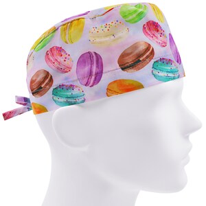 Op de afbeelding: Een paarse, witte en roze chirurgische scrub-muts met een kleurrijk macaron-patroon.