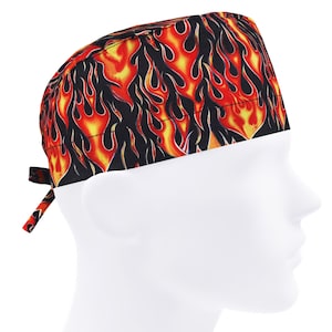 May include: A scrub cap featuring a flame pattern in red, yellow, and black. The cap has a tie closure at the back. The flame design is printed across the entire cap. This cap is designed for use in medical or professional environments.