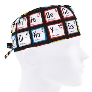 May include: A black surgical scrub cap featuring a periodic table design. The cap displays various element symbols and atomic numbers in white boxes against a black background. The cap has a tie in the back for adjustment.