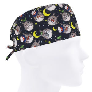 Op de afbeelding: Een donkerblauwe chirurgische scrubcap met een herhalend patroon van stripfiguren, maanvormen en sterren. De cap heeft bandjes aan de achterkant voor een verstelbare pasvorm. Het ontwerp bevat karakters met rode, witte en blauwe accenten.