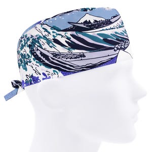 May include: A patterned surgical scrub cap featuring a Japanese wave design in shades of blue, white, and teal. The cap has a tie closure at the back and is worn on a mannequin head. The design includes boats and a mountain.